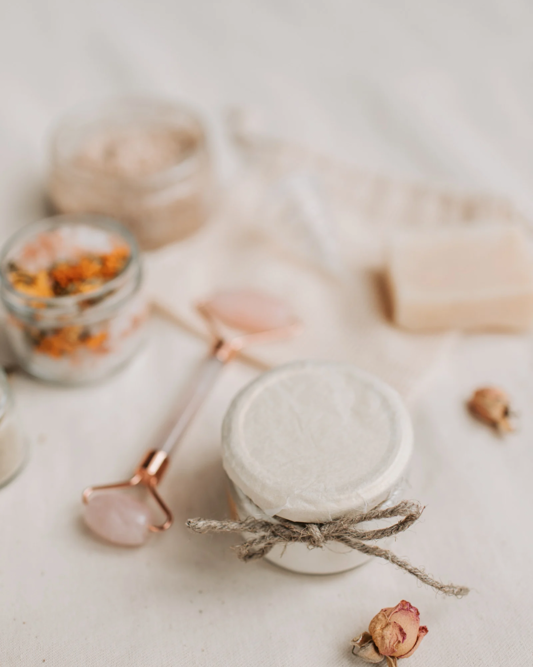 Soft neutral wellness flat lay featuring a rose quartz facial roller, natural skincare elements, and spa-inspired self-care accessories on a cream background